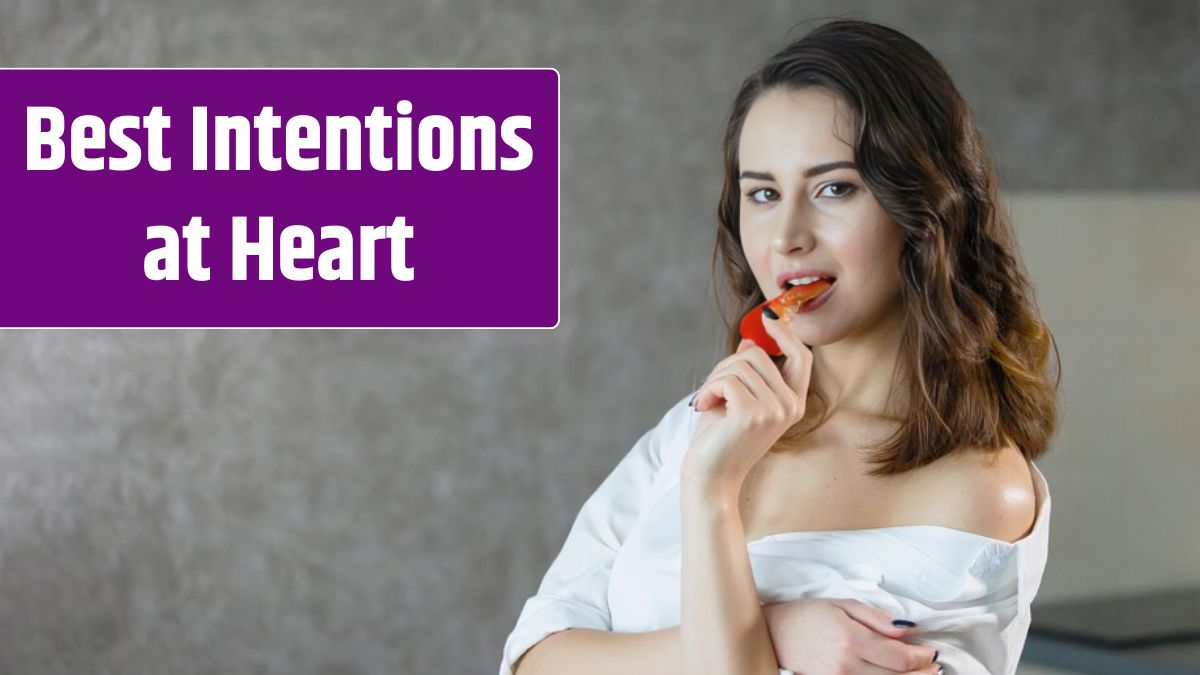 One young pretty woman in a white shirt in the kitchen is eating red pepper and smiling.