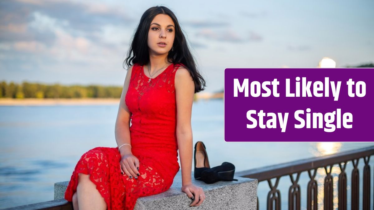 A girl in a long red dress is sitting on the fence of the river embankment.