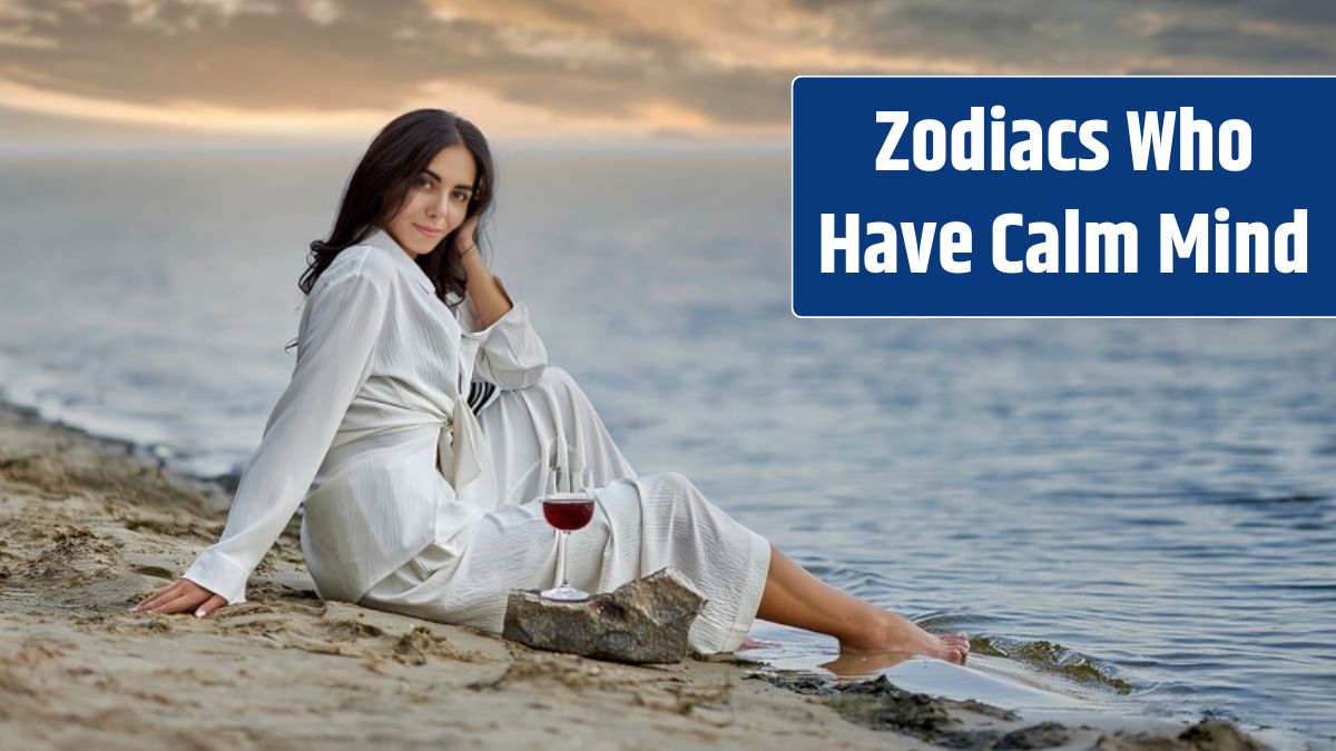 A beautiful girl in a white suit with a glass of red wine sits on the beach at sunset.